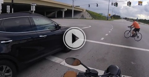 A cyclist crossing the road in front of a motorbike and car.