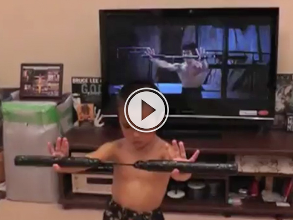 A kid giving the same pose as Bruce Lee on the TV behind him, titled 'Meet Bruce Lee's Mini'. (VIDEO)