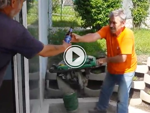 Man in orange tee and blue jeans accepts a bottle of beer from another man!