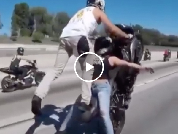 Woman balances on motorcycle as man pops a wheelie in tandem stunt